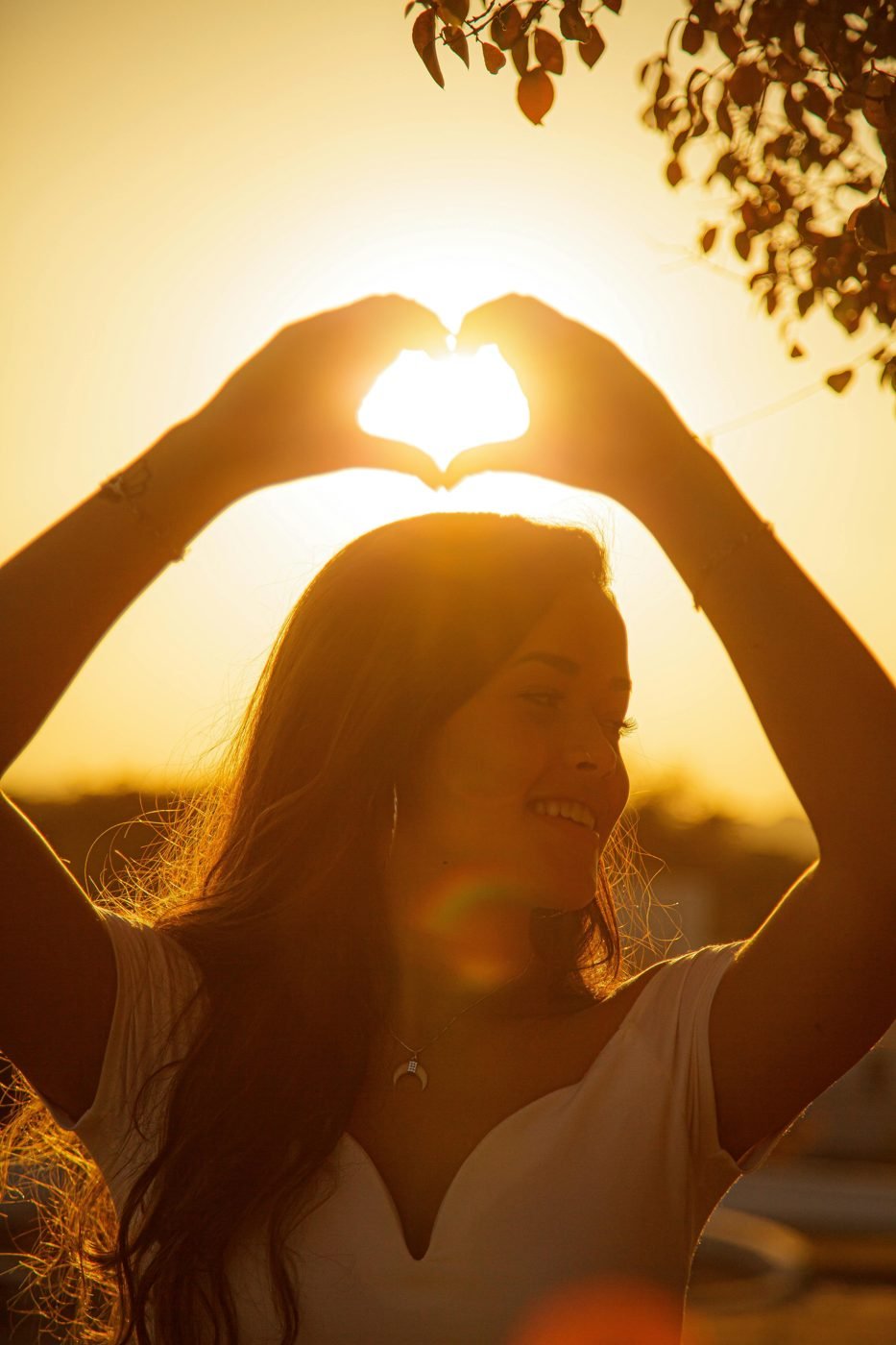Mujer formando un corazón con las manos frente al sol